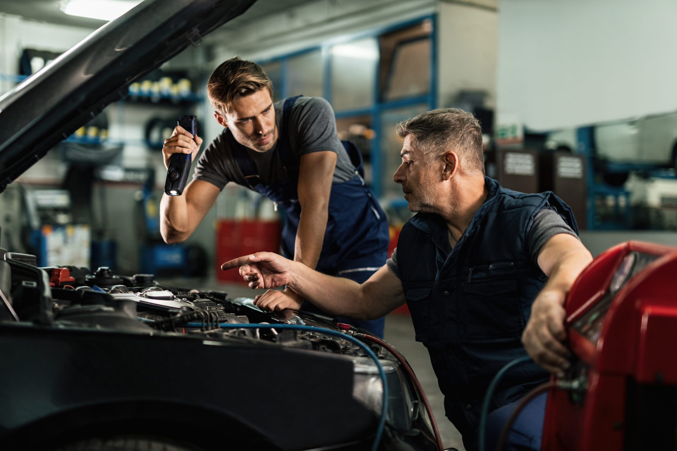 Two mechanics talking while repairing car's AC unit in auto repair - Haulogis